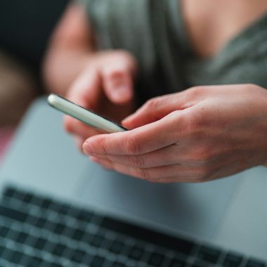 Hände bedienen ein Smartphone neben einem Laptop – Symbolbild für externe Mitarbeiterberatung